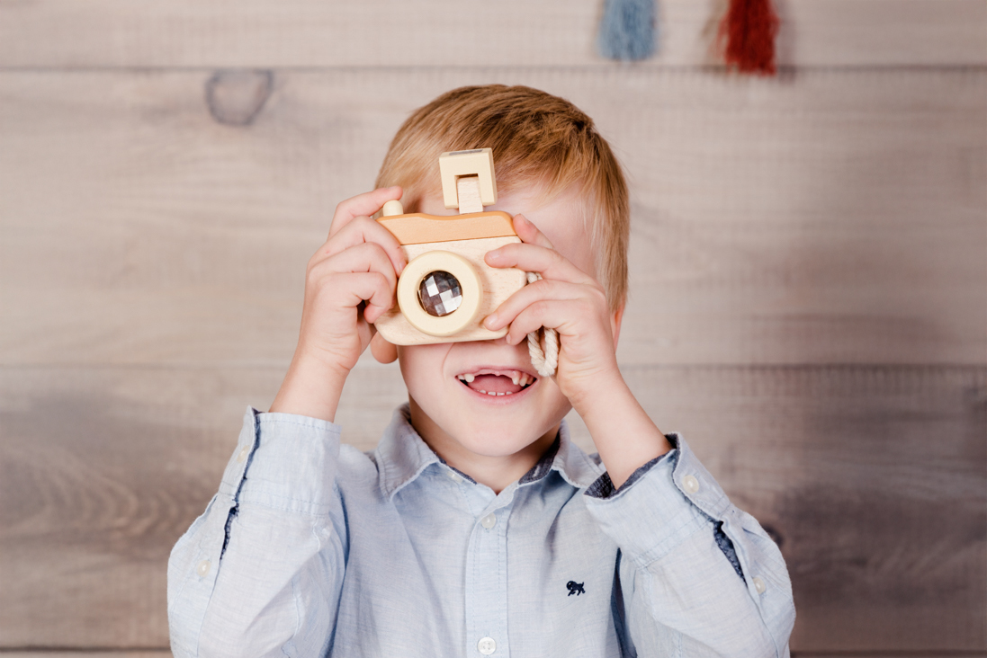 Kindergartenfoto eines Jungen mit einer Spielzeug Kamera vorm Gesicht