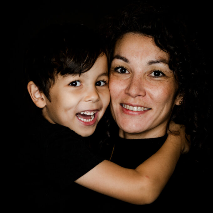 Portraitfoto einer Mama mit ihrem Sohn, schwarzer Hintergrund, beide lachen in die Kamera