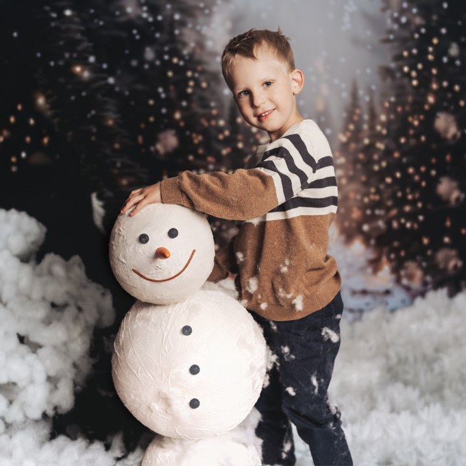 Ein Junge mit einem Schneemann in einer weihnachtlichen Schnee-Wald-Landschaft
